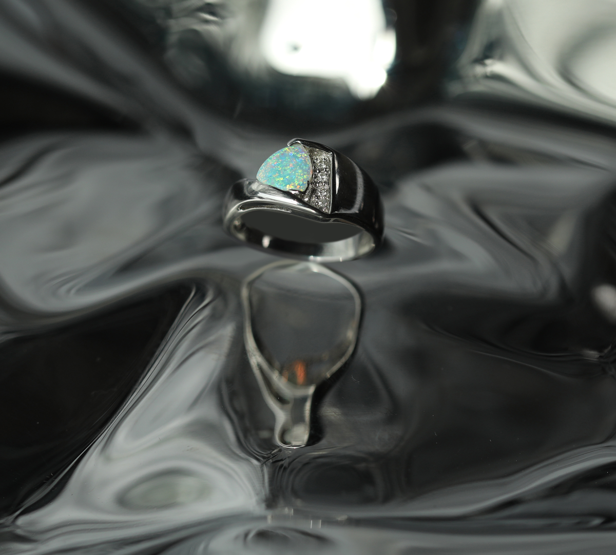 White gold ring set with a light opal and diamonds, resting on rippled black.